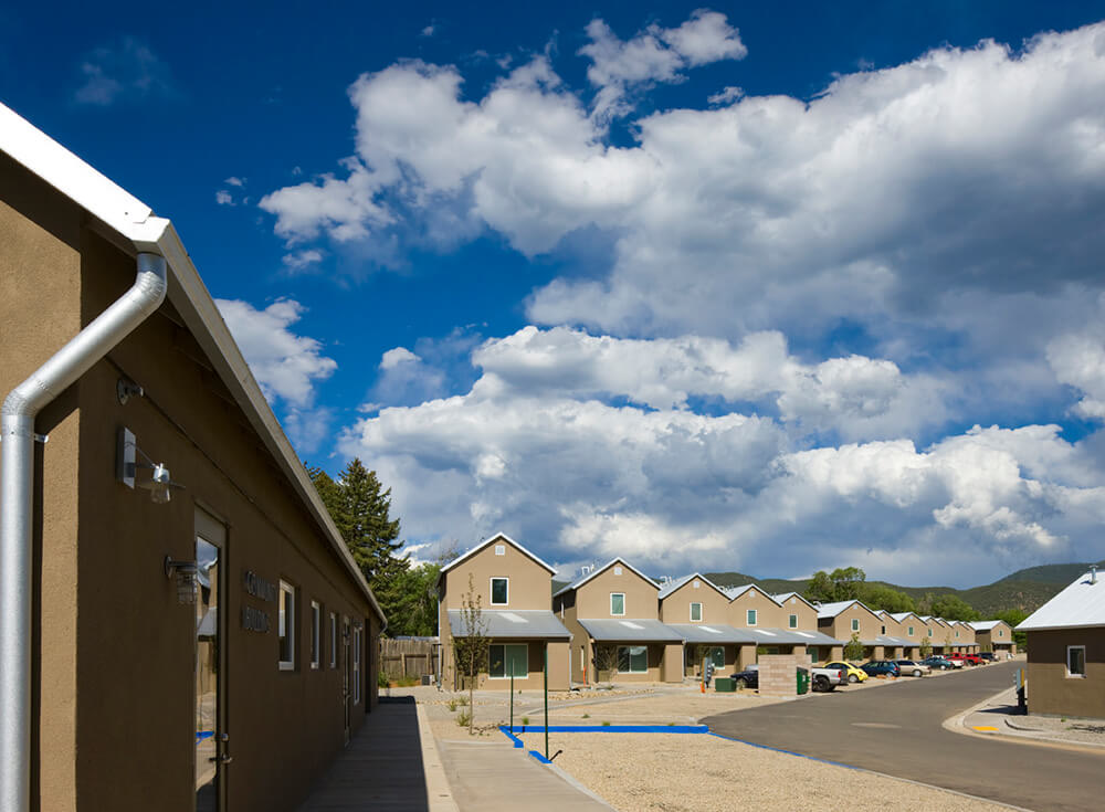 Community street at Taos Haus with detached homes, gravel yards, and green hills beyond